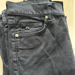  J.Lindeberg jeans - Svarta jeansbyxor från J.Lindeberg med klassisk femficksdesign och diskret logga på myntfickan. Byxorna har raka ben och är tillverkade i ett mjukt bomullsmaterial med lite stretch för extra komfort. Perfekta för en clean och stilren look.