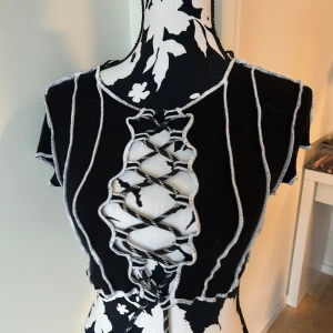 Svart snörad croppad topp Divided - Svart croppad topp från Divided med vita kontrastsömmar och cool snörning framtill. Toppen har korta ärmar och ribbad struktur. Den har inte blivit använd på väldigt länge och har kanske använts 3 ggr totalt. Orginelt från H&M