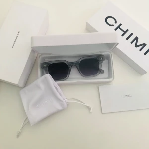 Grå transparenta solglasögon CHIMI - Snygga solglasögon från CHIMI med transparent grå båge och fyrkantig form. Sidorna har en diskret CHIMI-logga i silver. Kommer med originalfodral och påse. Perfekt accessoar för att lyfta din stil i sommar.