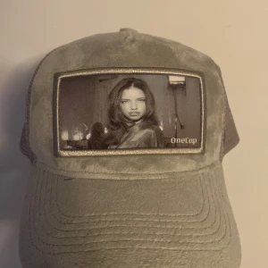 Grå keps från OneCap med fototryck (intresskoll) - Snygg grå keps från OneCap med mjuk sammet framtill och mesh på sidorna. Framsidan har ett stort svartvitt fototryck och broderad logga. Justerbar passform och cool streetstil, perfekt för att sticka ut.