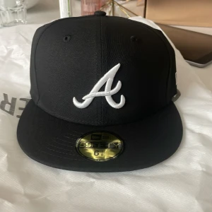 Svart New Era 59FIFTY fitted keps Atlanta braves - Helt ny, lappar och allt är kvar. Har kvitto om man vill se. Aldrig använd. Skick 10/10. Svart New Era 59FIFTY keps med Atlanta Braves-logga broderad i vitt framtill och MLB-logga bak. Klassisk flat peak och stilren look, perfekt för dig som gillar sportig streetstyle. Tillverkad i tåligt material och sitter snyggt på huvudet. 54,9 cm är storleken. Nypris 500+ frakt, men är slutsåld nästan överallt.