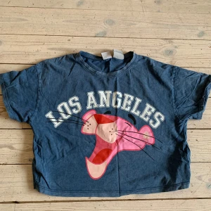 Blå Pink Panther topp/magtröja från Zara - Den har använts fåtal gånger. Snygg blå topp/magtröja från Zara med Pink Panther-tryck och texten 'Los Angeles' på bröstet. Modellen är croppad och har korta ärmar. Perfekt för dig som gillar coola prints och vill sticka ut lite extra. Materialet är mjuk bomull som känns skönt mot huden. 