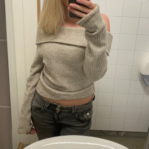 Beige ribbad offshoulder stickad tröja - Går att pruta!!!! Superfin beige stickad tröja med ribbad struktur och offshoulder-modell. Tröjan är croppad och har långa ärmar som sitter lite löst. Perfekt för dig som gillar en chill men ändå snygg stil.