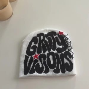 Vit mössa med tryck - Vit mössa med stor svart text och röda stjärnor framtill. Ena sidan har ett coolt spindelnätsmönster i svart. Mjuk och stretchig, perfekt för dig som gillar streetstyle och unika detaljer.