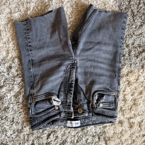Grå raka jeans från Zara - Snygga grå jeans från Zara med raka ben och klassiska femficksdetaljer. Jeansen har dragkedja och knapp framtill samt stora bakfickor. Perfekta till en avslappnad streetstil.