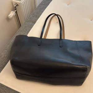 Svart skinnväska från Åhléns - Stilren och rymlig väska i svart skinn från Åhléns  med långa handtag och ljusbrunt innerfoder. Väskan har innerfack för småprylar och en minimalistisk design som passar perfekt till vardagslooken och universitet/skola eller en weekend get away💕