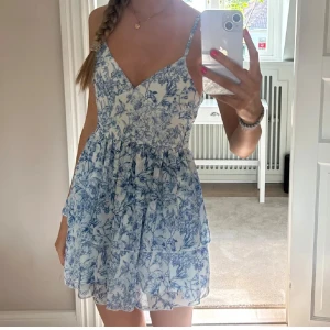 Blåvit blommig kortklänning - Superfin kortklänning med blått blommönster på vit botten. Klänningen har smala axelband, v-ringning och volangig. Köpte klänningen av en tjej men storleken var för liten där av vet jag inte märket🩵🩵🩵🩵