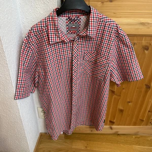 Rutig kortärmad skjorta Mountain Life - Kortärmad skjorta från McKinley i rött, vitt och blått rutigt mönster. Klassisk krage, bröstficka och knäppning framtill. Skön och luftig modell i bomull.