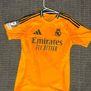 Real Madrid Mbappé fotbollströja orange - Snygg orange Real Madrid fotbollströja från Adidas med Mbappé och nummer 9 på ryggen. Perfekt för sommaren och fotbolls eventer. Pris kan sänkas. OBS: Inga Barcalona fans