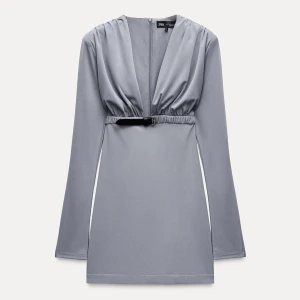 Grå kortklänning från Zara - Supersnygg grå kortklänning från Zara med djup v-ringning, långa ärmar och ett coolt bälte i midjan. Klänningen har en stilren och modern look, perfekt för dig som gillar minimalistisk stil.