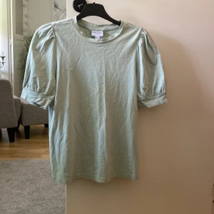 Ljusgrön topp med puffärm från Aware - Superfin ljusgrön topp från Aware med puffiga korta ärmar och rund halsringning. Tillverkad i mjuk bomull som känns skön mot huden. Perfekt för dig som gillar en enkel men ändå trendig look med lite volym på axlarna.