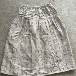 Beige blommig kortkjol från Zara - Supersöt beige kortkjol från Zara med band på sidorna  och små blommiga mönster. Kjolen  har rynkade detaljer upptill och är gjord i ett luftigt linnematerial, perfekt för varma dagar. Snygg och enkel att styla till sneakers eller sandaler.