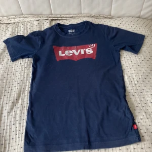 Mörkblå Levi's t-shirt med logga - Snygg mörkblå t-shirt från Levi's med klassisk röd och vit logga på bröstet. T-shirten har rund hals, korta ärmar och är gjord i mjuk bomull. Perfekt för en avslappnad och cool stil.