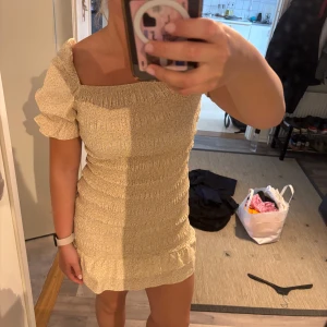 Smockklänning från NAKD - Gul smockklänning från NAKD, sitter som en smäck men tyvärr vuxit ur den! Volang nedtill samt puffärmar. Ärmarna kan man ha antingen som på bild eller justera som one shoulder. Storlek 38!