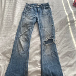 Ljusblå bootcut jeans från Zara - Snygga ljusblå bootcut jeans från Zara med slitningar och en fläck av blekningsmedel på ena benet. Klassisk femficksmodell med dragkedja och knapp. Jeansen har en avslappnad vibe och är tillverkade i bomull med en skön passform.