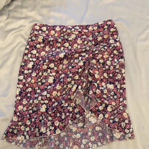 Blommig volangkjol från SHEIN - Supersöt blommig kjol från SHEIN i storlek S. Kjolen är kort med volangkant och har ett färgglatt blommönster i rosa, vit, gul och blå. Omlottstil framtill ger en extra snygg touch. Perfekt för dig som vill sticka ut lite extra i sommar!