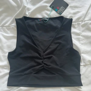 Svart croppad topp Even&Odd - Svart croppad topp från Even&Odd med snygg v-ringning och twistad detalj framtill. Ärmlös och perfekt att styla med höga jeans eller kjol. Enkel men trendig design som passar till många looks