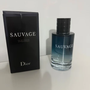 Dior Sauvage Eau de Toilette - Dior Sauvage Eau de Toilette med stilren, cylindrisk glasflaska i mörkblått som tonar mot klart. Svart, glansig kork med Dior-logga på toppen. Kommer med original svart kartong med vit text. En ikonisk och fräsch herrdoft.