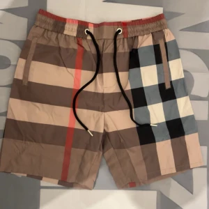 Rutig shorts med snörning - Snygga shorts med klassiskt rutigt mönster i beige, brunt, svart, vitt och rött. De har elastisk midja med svart snörning och sidofickor. Perfekta för sommaren och ger en trendig vibe till din outfit.