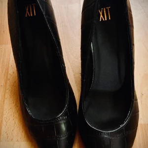 Svarta pumps i krokodilmönster från XIT! - Svarta pumps i krokodilmönster i storlek 41 från XIT. Klackhöjd 5 cm. I skick som nya.