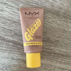 NYX Buttermelt Glaze Skin Tint - Helt ny, NYX Buttermelt Glaze Soft Glow Skin Tint i nyansen 03 Cashew Butta. Ger en naturlig glow och lätt täckning, med SPF 30. Innehåller niacinamid, mango och sheasmör. Tuben rymmer 30 ml och har gul kork.