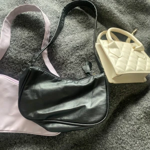 Axelväskor i olika färger  - Säljer tre snygga väskor: en svart axelväska i skinnimitation med dragkedja, en quiltad beige handväska med korta handtag och en ljuslila axelväska i mjukt material. Perfekta accessoarer för att lyfta din outfit och matcha olika stilar. Varsågod och köpa🥰