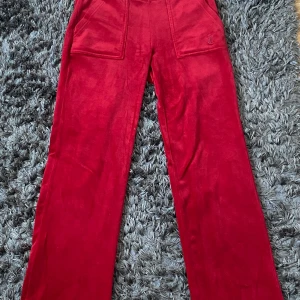Röda velourbyxor Juicy Couture XS - Röda mjukisbyxor från Juicy Couture i velour med breda raka ben, stora fickor fram och bak samt snörning i midjan. Klassisk logga broderad på ena fickan. Perfekta för en chill och trendig look.