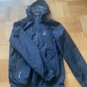 Svart vindjacka från haglöfs  - Svart vindjacka från Haglöfs i storlek M. Jackan har huva, dragkedja framtill och två fickor med dragkedja. Tillverkad i slitstark polyester med meshfoder och GORE-TEX-detalj. Perfekt för blåsiga dagar och outdoor vibes. Har använt den typ 2 gånger så väldigt bra skick