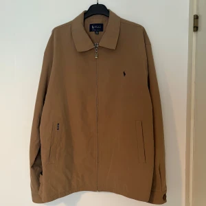 Beige vindjacka från Polo Ralph Lauren - En sjukt fin och efterfrågad Ralph Lauren jacka, den passar dig som bär L, den är ljusare i verkligheten!! Det är fint att ha en hoodie men och också en t shirt under. Cond 9/10, den är köpt i New York. Inga defekter! Hör av dig vid frågor eller funderingar!