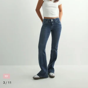 Nelly jeans - Säljer ett par mörkblå bootcut jeans med klassisk femficksdesign och vita kontrastsömmar på bakfickorna. Jeansen har normal passform och stängs med dragkedja och knapp. Perfekta för dig som gillar en tidlös och snygg look. Använda 1 gång där av pris. Ny pris 699kr