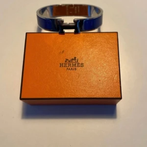Blått H armband  - Ett blått H armband med original förpackning och helt ny.