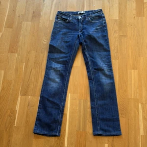 Blå jeansbyxor från Acne Jeans - Klassiska blå jeansbyxor från Acne Jeans med slim fit och femficksdesign. Byxorna har en slim passform och stängs med knapp och dragkedja. Perfekta för en avslappnad stil och funkar året runt. Storlek 28/32 men sitter som 28/30.