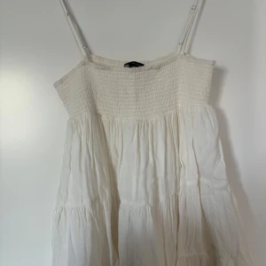 Vit sommarklänning från Zara - Säljer en vit klänning från Zara med smock upptill och tunna axelband. Klänningen har en luftig och flowy passform, perfekt för varma dagar. Säljes endast för att den inte kommer till användning längre. Men i väldigt fint skick och väldigt sparsamt använt. 