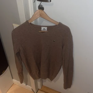 Beige tröja från Lacoste - Säljer en stilren beige tröja från Lacoste med det klassiska krokodilmärket på bröstet. Tröjan har långa ärmar och en rund halsringning. Perfekt för en avslappnad och snygg look. Osäker på storlek men skulle säga att den passar nån som bär Xs