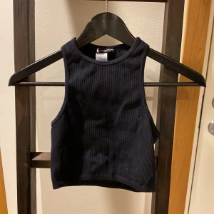 Svart ribbad croppad linnetopp Zara  - Säljer en svart ribbad croppad linnetopp med hög hals. Toppen är ärmlös och har en tight passform, perfekt för sommaren. Enkel och stilren design som passar till många olika outfits.