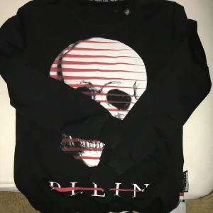 Svart långärmad tröja med dödskalle från Philipp Plein - Cool svart långärmad tröja från Philipp Plein med stor vit och röd dödskalle-tryck på framsidan och logga i nacken. Perfekt statement-piece (äkta)