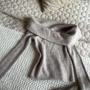Beige ribbad offshouldertröja - Säljer en beige ribbad tröja med bred offshoulder-krage. Tröjan har lång ärm och är figurnära i modellen. .