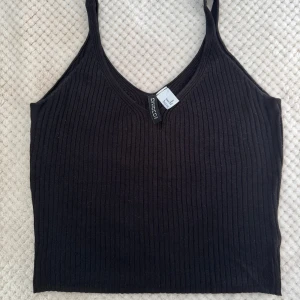 Ribbad topp  - Svart ribbad linnetopp med smala axelband och v-ringning. Perfekt att styla till olika outfits och enkel att matcha med både jeans och kjol.