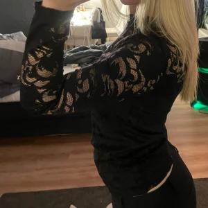 Svart spetsblus från Vila - Säljer en svart långärmad spetsblus från Vila i storlek XS. Blusen har transparenta partier med blommigt spetsmönster och hög hals. Perfekt för dig som vill ha en snygg och stilren topp med det lilla extra.