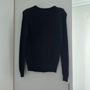 Svart stickad tröja - Säljer en svart stickad tröja med rund halsringning och långa ärmar. Tröjan har en klassisk passform och ribbade muddar vid ärmslut och nederkant. Perfekt för kyligare dagar och enkel att matcha med olika outfits.
