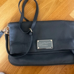 Grå axelväska från Marc by Marc Jacobs - Säljer en grå axelväska från Marc by Marc Jacobs i äkta skinn. Säljer en billigt pågrund av att ens knappen/ niten som ni kan se närmare på bild 3 är av. Det går enkelt att fixa hos en skomakare. Går att pruta ner priset lite om så fallet!