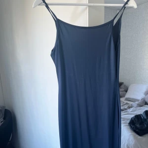 Mörkblå långklänning med smala axelband - En stilren mörkblå långklänning med smala axelband och rak siluett. Klänningen har en minimalistisk design och är tillverkad i ett mjukt, stretchigt material som ger en bekväm passform. Perfekt för sommarens varma dagar. Köpt i Italien på nå marknad så vet ej märke