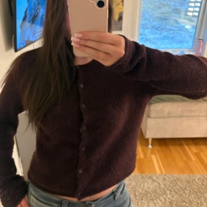  Gina Tricot kofta - Säljer en mysig vinröd kofta från Gina Tricot i storlek M. Koftan har långa ärmar, knappar framtill och är tillverkad i ett fluffigt, stickat material. Perfekt för lager-på-lager och en snygg vardagslook.