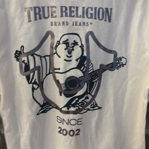 Vit t-shirt från True Religion - ”Big HS Foil Buddha Tee” från True Religion med metallicfärgat logotryck på bröstet och stort tryck på ryggen. Helt ny med tag! 