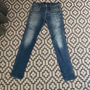 Replay hyperflex - Säljer ett par blå jeans från Replay med snygga slitningar och klassisk femficksdesign. Jeansen har smal passform och normal midja, perfekt för en avslappnad men stilren look. Märkeslapp bak och diskreta detaljer framtill.