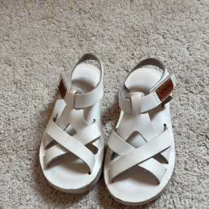 Vita sandaler från Kavat - Säljer ett par vita sandaler från Kavat med klassisk design och breda remmar. Skorna har en justerbar rem med kardborre och öppen tå. Perfekta för varma dagar och enkel att ta på och av.