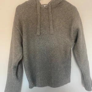 Grå stickad hoodie från ZARA - Mysig grå stickad hoodie från ZARA med huva och dragsko. Tröjan har långa ärmar och bred ribbad kant nedtill och vid ärmsluten. Perfekt för kyliga dagar och enkel att matcha med olika outfits.