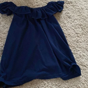 Marinblå offshoulder klänning från H&M - Söt marinblå klänning från H&M med volang upptill och offshoulder-design. Perfekt för sommarens varma dagar. Klänningen har en lös passform och är tillverkad i mjukt material.