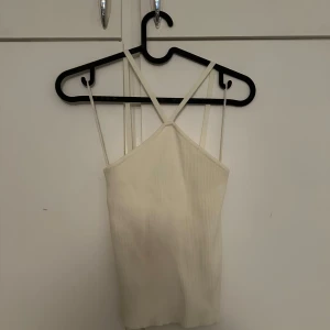 Vit ribbad linnetopp från Vero Moda - Säljer en vit ribbad linnetopp från Vero Moda med smala axelband som korsas fram till. Toppen har en croppad passform och är perfekt för varma dagar. Enkel och stilren design som passar till mycket.