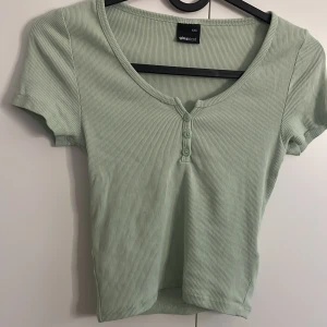 Ljusgrön ribbad topp från Gina Tricot - Säljer en jättegullig ljusgrön ribbad topp från Gina Tricot i storlek XXS. Toppen har korta ärmar, v-ringning och tre knappar framtill🤍säljer då den inte kommer till användning längre🤍 